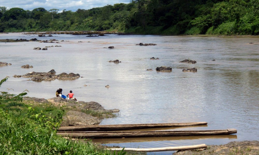 Río tropical con personas sentadas en orilla, canoas en primer plano